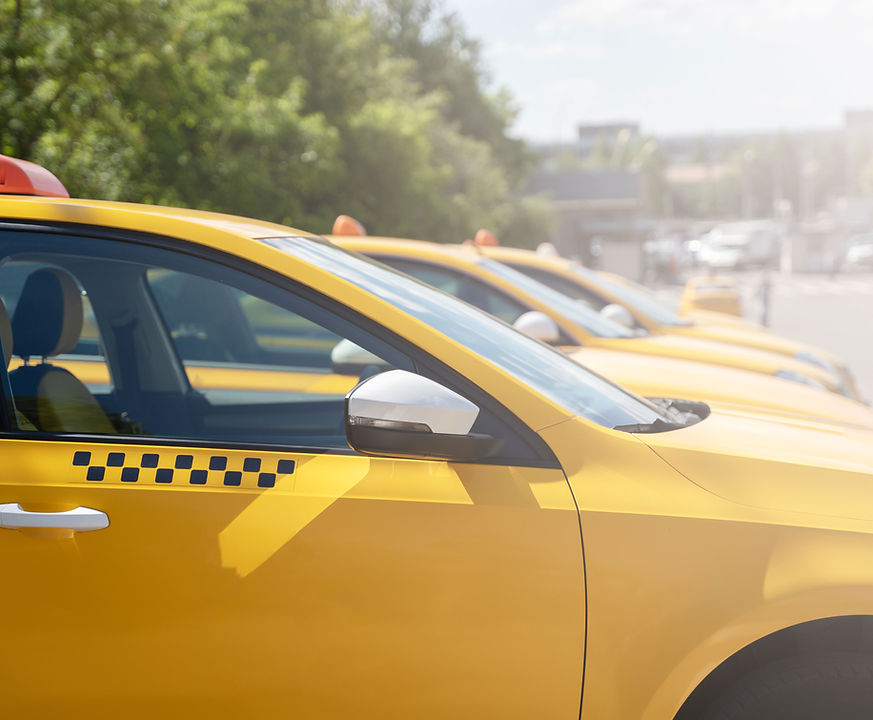Row of bright yellow taxis parked along a sunny street. Each car has a checkered design on the side, conveying a busy urban atmosphere.
